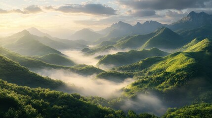 Obraz premium Lush green mountains under a cloudy sky, with mist drifting through the valleys, creating a serene and tranquil landscape.