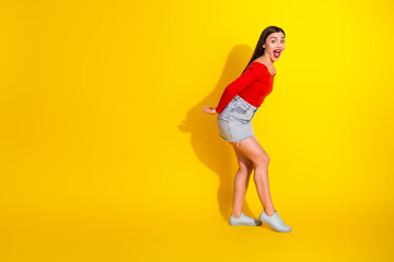 Young woman in a red shirt and denim skirt posing joyfully against a vibrant yellow backdrop