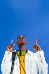 Young student pointing upwards with index fingers on blue background