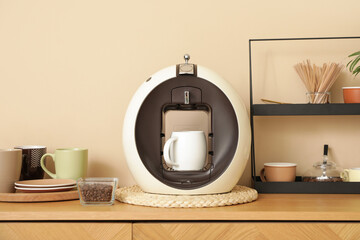 Modern coffee machine with cups and bowl of beans on counter in kitchen