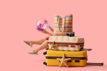 Female tourist with beach ball and suitcases on pink background