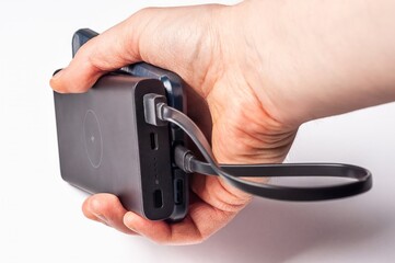 A hand is holding a smartphone connected to a portable power bank with a charging cable.