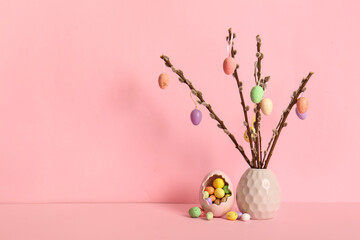 Vase with willow branches and colorful Easter eggs on yellow background