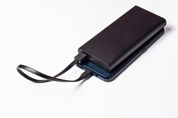A black power bank charges a blue smartphone via USB, providing a convenient portable power...