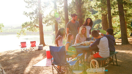 Two Familes Having Picnic Camping By Lake On Hiking Adventure In Forest