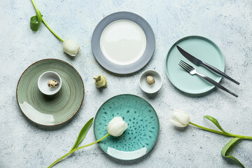 Different clean plates with quail eggs, toy bunny and beautiful tulip flowers on white background....