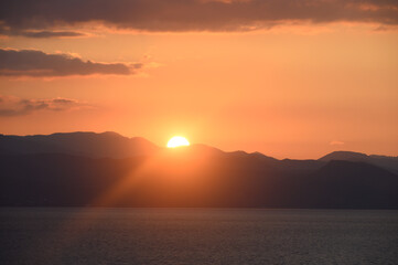 Golden sunset casts a warm glow over tranquil mountains and serene waters in a picturesque landscape