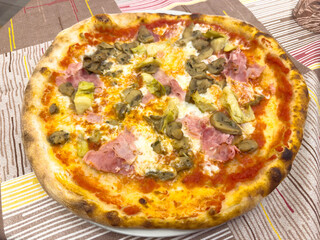 Delicious italian pizza with mushrooms, ham, and artichokes on a colorful tablecloth