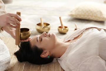Fototapeta na wymiar Woman undergoing singing bowl therapy lying on floor indoors