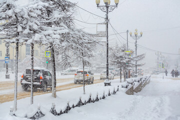 Snow covered city street. Pedestrian looks at the road where the cars go. Lots of snow after a snowfall. Cold snowy weather. Bad visibility. Magadan, Magadan Region, Siberia, Russia.