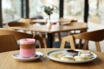 Delicious cottage cheese pancakes and pink latte served on wooden table indoors