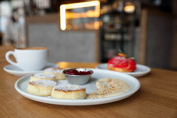 Delicious cottage cheese pancakes, dessert and coffee served on wooden table in cafe, closeup