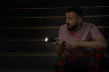 Fear of darkness. Scared man with flashlight indoors at night, space for text