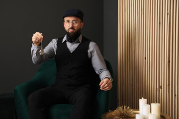 Hypnosis session. Man with vintage pocket watch in armchair near grey wall indoors