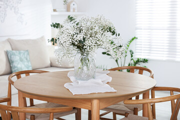Bouquet of beautiful gypsophila flowers and eucalyptus branches in vase on dinner table indoors
