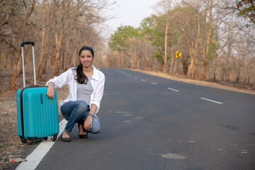 Happy Indian solo traveler with her stroller or bag waiting roadside
