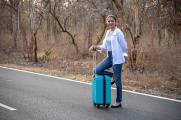 Happy Indian solo traveler with her stroller or bag waiting roadside
