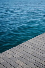 Fototapeta premium there is a brick walkway next to the water with a boat in the background