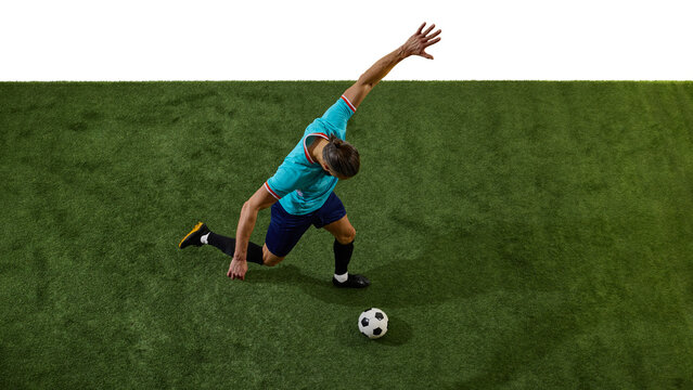 Overhead view of footballer in blue uniform preparing to strike ball, body leaning forward, arms extended for balance on green field. Concept of tactics, technique, teamwork, championship, precision. - Powered by Adobe