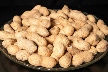 Peanuts in shell on glass plate close-up. Black background.