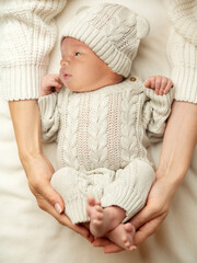 Baby lying on Blanket in Mother Hands. Mum Love. Newborn sleep in woolen Bodysuit in Parent embrace. Infant Clothes. Little Child Development