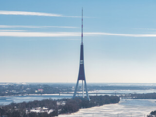 The Riga TV Tower stands on an island in the Daugava River, surrounded by snow and frozen water,...