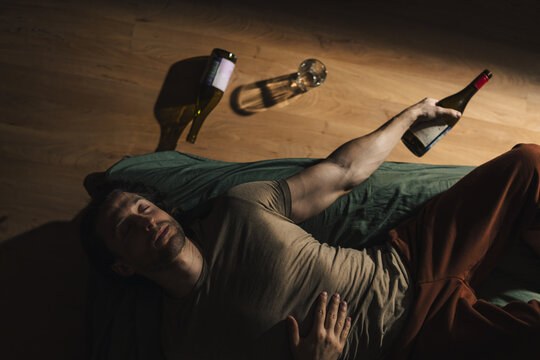 A man lies on a bed with empty alcohol bottles next to him