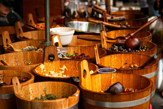 a street market stall selling fresh organic olives, pesto, hummus and dried tomatoes in wooden barrels