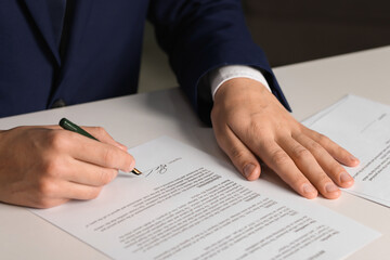 Man putting signature on document at white table, closeup