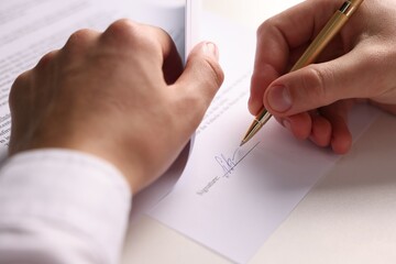 Man putting signature on document at white table, closeup