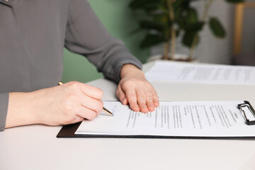 Woman putting signature on document at white table, closeup