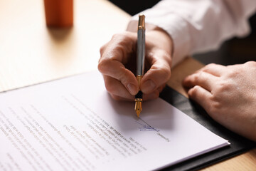 Woman putting signature on document at table, closeup