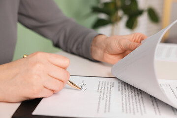 Woman putting signature on document at table, closeup