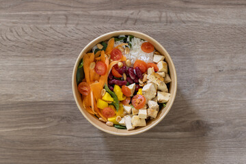 Top-down view of a nutritious salad bowl with grilled chicken, rice, cherry tomatoes, carrots, beans, mango, peanuts, and fresh greens. Served in an eco-friendly bowl with a take-away presentation.