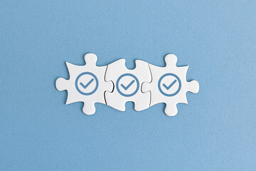 Three white puzzle pieces with white checkmarks are arranged in a row on blue background. represents  completion or agreement, problem-solving, validation, teamwork, and strategic thinking.