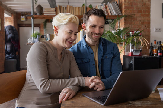 Couple at home smiling as they apply for a home loan on a laptop