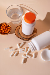 Nutraceuticals, health care. Glass of water, vitamins, capsules, dietary supplements, probiotics, tablets, white jar container on beige background with beautiful long shadows. Medical background