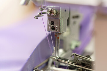Processing textile fabric on a sewing machine, close-up of threads and needles.