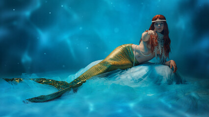 Enticing gesture. Redhaired mermaid with shimmering golden tail floating in soft blue light,...