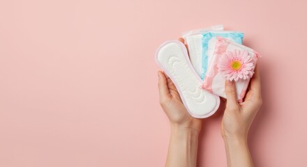 A person holding a sanitary pad and packaged hygiene products with a decorative pink flower on a soft pink background