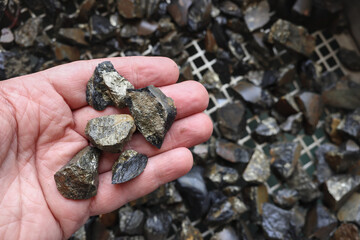Mine, mining of tin (Sn) ore, as mineral cassiterite (SnO2). Rocks held in hand. Element used in Lithium-ion batteries, coils of superconducting magnets, pigments, solder, plating and bronze metal