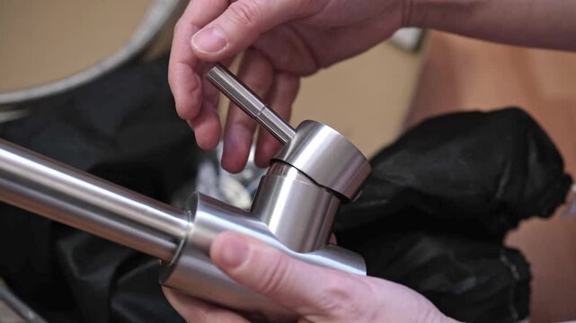 Close-up of hands adjusting a stainless kitchen faucet. Checking the serviceability of a single-valve kitchen faucet.