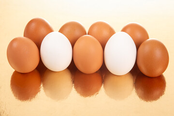 A collection of white and brown eggs on a glossy golden background, casting soft reflections in a simple yet striking food photography scene.