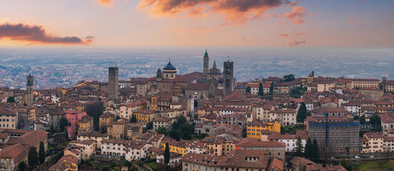 View of Bergamo's old town, Italy, at sunset, featuring the Basilica of Santa Maria Maggiore, medieval bell towers, and terracotta rooftops.