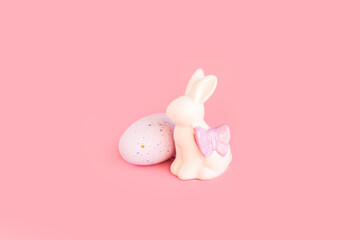 Happy easter decoration with white bunny decorative statuette and colorful eggs. Minimal festive composition on light patel pink background. Copy space, place for text, front view