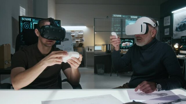 Medium shot of two male automotive engineers working together on new concept car using virtual reality headsets, holding clay model and manipulating digital visualization with handheld control