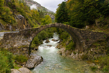 Puente románico de piedra sobre un río caudaloso, rodeado de vegetación en Isaba, Navarra,...