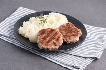 Savory grilled patties with creamy mashed potatoes and fresh rosemary on a dark plate