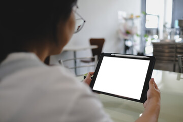 Woman using a digital tablet with blank screen and stylus in a modern cafe, focusing on note-taking...