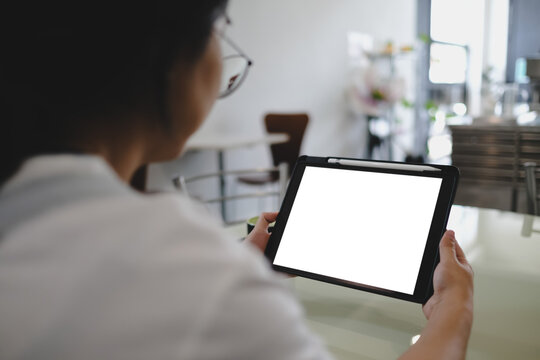 Woman using a digital tablet with blank screen and stylus in a modern cafe, focusing on note-taking or creative work.